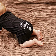 Zuhan is registered to the contest to win money with this photo: baby, blonde_hair, black_onesie, lightbulb_graphic, crawling, knitted_blanket, cozy, cute, infant, child, soft_texture, indoors, floor, barefoot, pattern, warm_colors, toddler, young_child, clothing, baby_pose