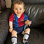 Badis participe au concours pour gagner de l'argent avec cette photo : baby, child, clothing, couch, curly_hair, cute, fc_barcelona, football_shirt, happy, home, indoor, jersey, leather, pacifier, person, shorts, sitting, smiling, socks, toddler