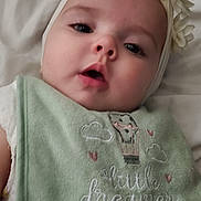 Mercee is registered to the contest to win money with this photo: baby, bib, blanket, child, clothing, cute, expression, face, flower, green, headband, indoors, infant, lying_down, portrait, sleepwear, soft, text, white, young