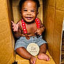 Jamal is registered to the contest to win money with this photo: baby, infant, smiling, cardboard_box, suspenders, striped_shorts, six_months, wooden_sign, waving_hand, barefoot, cute, happy, portrait, child, indoors, skin, face, expression, sitting, floor