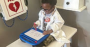 Jamal joined the competition — help win amazing prizes! child, doctor, white_coat, stethoscope, glasses, magnetic_doodle_board, table, cabinet, aed_box, drawing, indoor, toy, playing, person, medical_theme, young_child, camouflage_pants, black_hair, footwear, focused