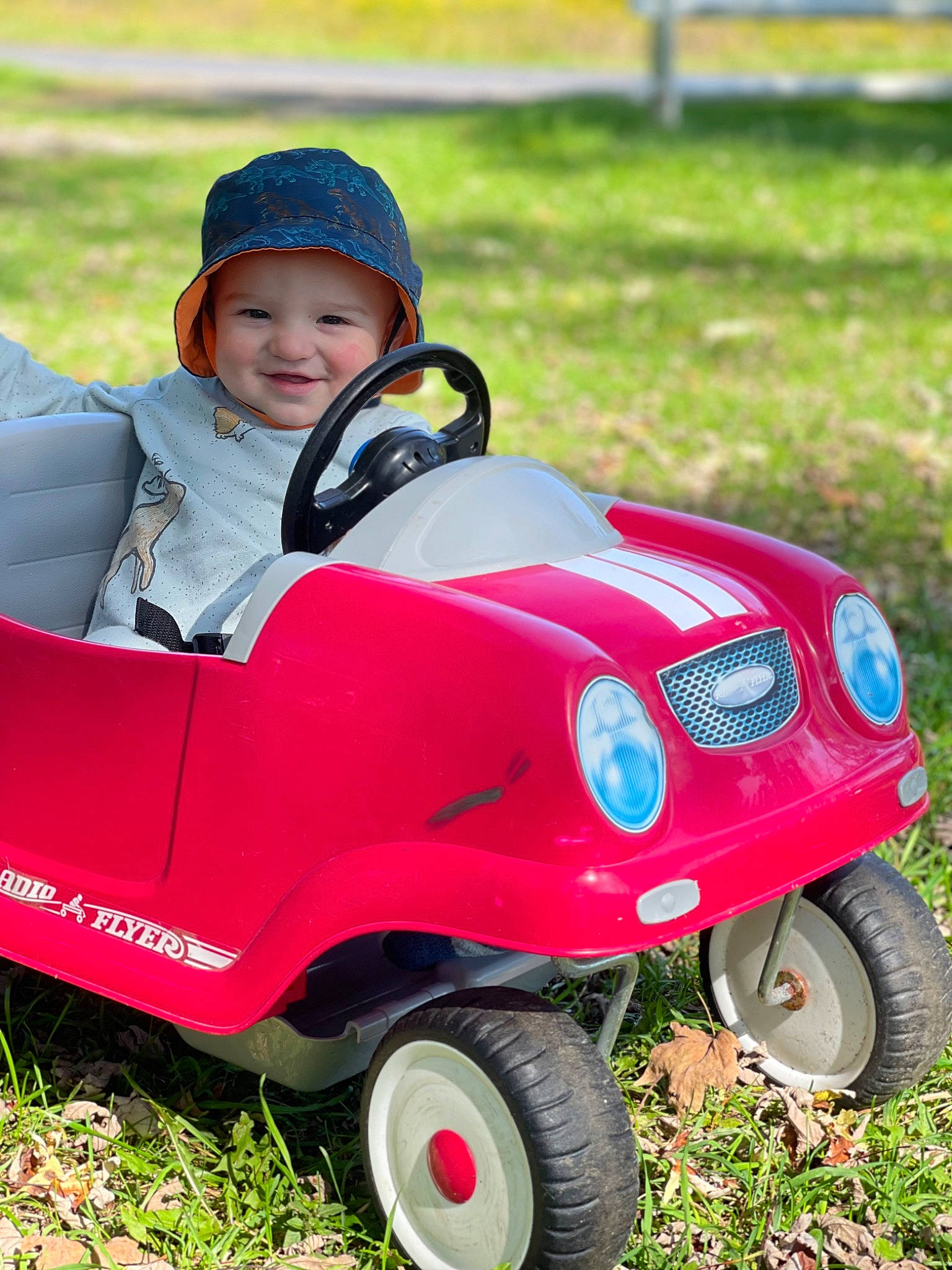Mason is registered to the contest to win money with this photo: automotive_design, automotive_tire, automotive_wheel_system, baby, baby_toddler_clothing, fun, grass, happy, headwear, helmet, joy, lawn, leisure, motor_vehicle, people_in_nature, person, plant, riding_toy, smile, tire