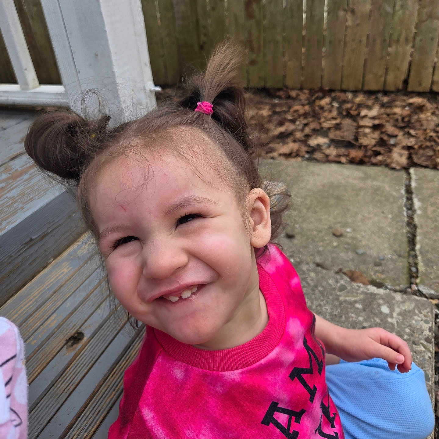 Freya joined the competition — help win amazing prizes! child, girl, pigtails, smile, outdoor, wooden_steps, fence, leaves, concrete, casual_clothing, pink_shirt, blue_pants, happy, portrait, person, sitting, daylight, playful, young, cute