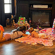 Iris is registered to the contest to win money with this photo: child, baby, toddler, blanket, tablet, floor, toy, book, television, wooden_floor, living_room, playtime, indoor, diaper, pink, socks, curtain, cross, decor, family