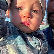 Maëlan participe au concours pour gagner de l'argent avec cette photo : adult, baby, beanie, beard, child, closeup, cute, expressionless, face, green_eyes, hand, headwear, outdoor, person, plaid_shirt, portrait, shadow, sunlight, toddler, warm_light