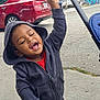 Legend is registered to the contest to win money with this photo: toddler, child, hoodie, smiling, happy, urban, sidewalk, car, graffiti, stroller, celebration, casual_clothing, sneakers, outdoor, person, joy, playful, hood, gesture, daytime