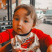 Quinn joined the competition — help win amazing prizes! toddler, child, indoor, high_chair, red_shirt, racing_cars, curly_hair, window, car, butterfly_emoji, playful, seated, cute, expression, wooden_furniture, daylight, casual_clothing, portrait, person, young_child