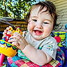 baby, child, toy, colorful, smiling, happy, curly_hair, face, outdoor, play, seat, infant, cute, person, closeup, daylight, joyful, expression, clothing, background