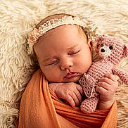 Louise a rejoint le concours — aidez-le/la à gagner de superbes lots ! baby, sleeping, swaddled, orange_wrap, pink_teddy_bear, crocheted_toy, headband, lace, blanket, fluffy, soft_texture, infant, cute, peaceful, portrait, closeup, hand, face, resting, indoor