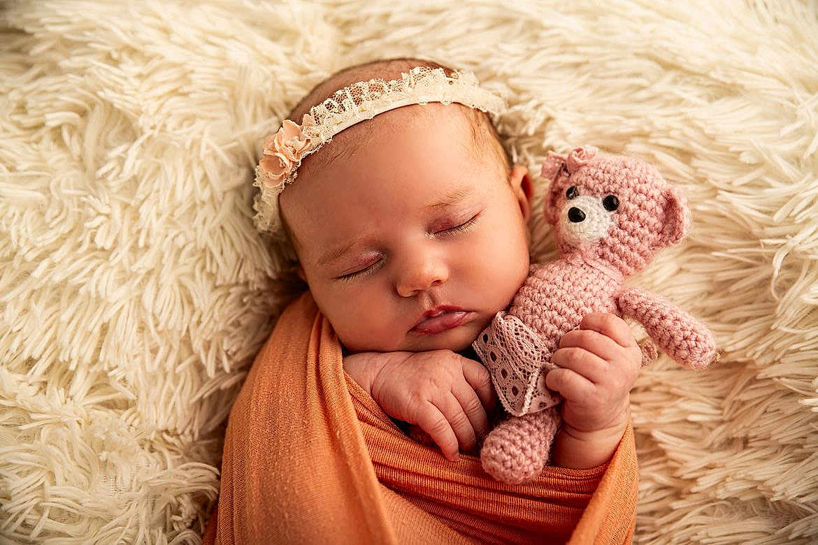 Louise a rejoint le concours — aidez-le/la à gagner de superbes lots ! baby, sleeping, swaddled, orange_wrap, pink_teddy_bear, crocheted_toy, headband, lace, blanket, fluffy, soft_texture, infant, cute, peaceful, portrait, closeup, hand, face, resting, indoor