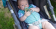 Clayton is registered to the contest to win money with this photo: baby, bottle, stroller, grass, outdoor, child, onesie, infant, legs, feet, blue, black_socks, seatbelt, relaxing, sunlight, person, summer, casual, young, cute