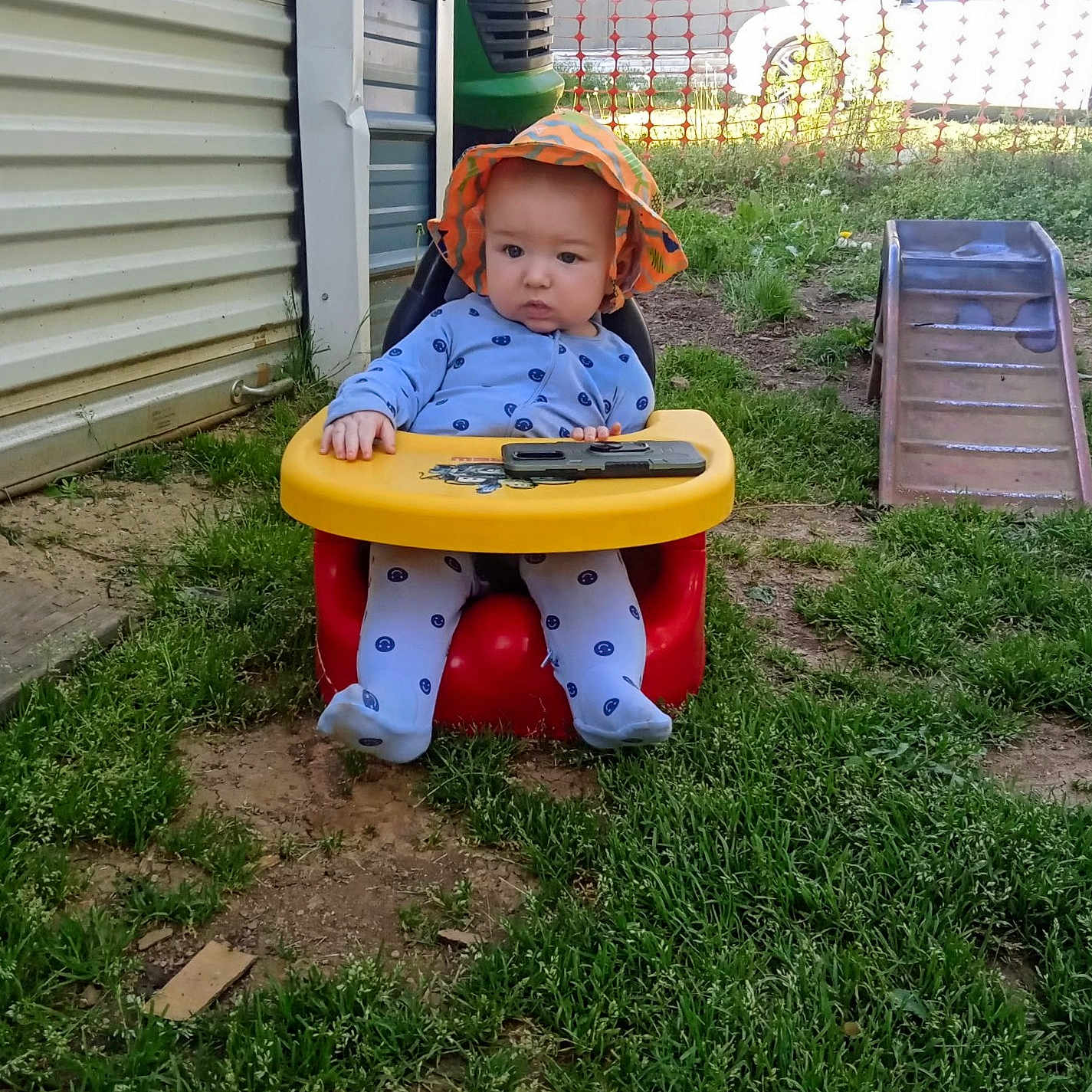 Clayton is registered to the contest to win money with this photo: baby, child, hat, sunhat, baby_seat, outdoor, grass, smartphone, slide, playground, car, fence, building, clothing, infant, curious, seat, toy, nature, daylight
