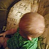 baby, child, blurry, grainy, green_clothing, head, patterned_cushion, indoor, infant, sitting, top_view, soft_fabric, wearing_clothes, young_child, human, skin, small_child, person, cushion, blurred
