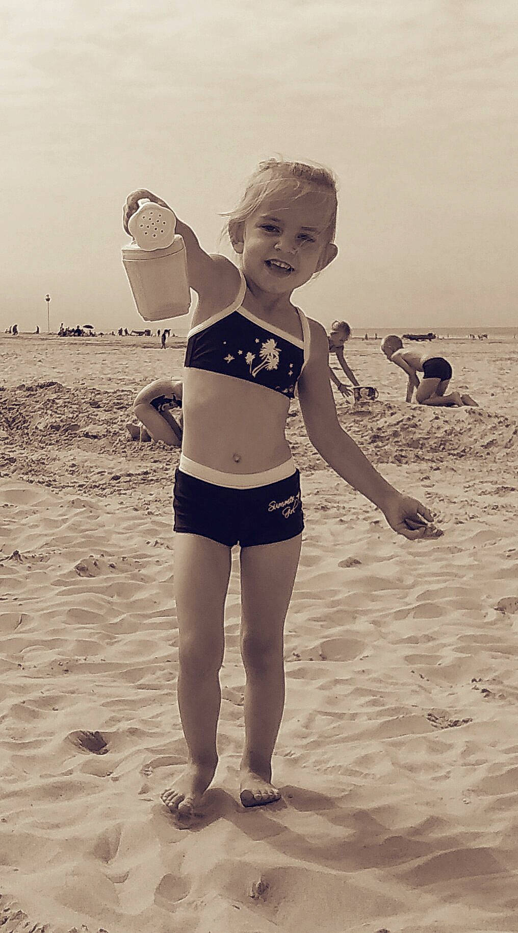 Noemie a rejoint le concours — aidez-le/la à gagner de superbes lots ! beach, black_and_white, child, fun, girl, happiness, joint, joy, leg, material, person, photograph, sand, sea, shorts, shoulder, standing, summer, sunglasses, swimwear