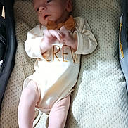 Aiden is registered to the contest to win money with this photo: baby, infant, onesie, bow_tie, baby_carrier, padded, clothing, skin, legs, hands, face, newborn, toddler, laying, indoor, soft, cute, small, child, person