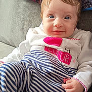 Elya a rejoint le concours — aidez-le/la à gagner de superbes lots ! baby, child, infant, blue_eyes, striped_pants, white_top, pink_heart, couch, indoor, portrait, cute, smile, hand, hair, face, seated, clothing, fabric, home, comfort