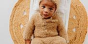 Dominic is registered to the contest to win money with this photo: baby, child, fuzzy_clothing, bear_costume, hat_with_ears, white_bed, pillow, woven_mat, round_mat, portrait, indoor, cute, cozy, soft_texture, infant, person, photography, sitting, expression, looking_at_camera