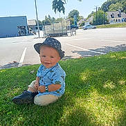Liam a rejoint le concours — aidez-le/la à gagner de superbes lots ! blue_shirt, building, car, child, dinosaur_print, grass, happy, hat, leaf, outdoors, parking_lot, portrait, shadow, shoes, sitting, smile, summer, sunhat, toddler, tree