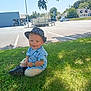 blue_shirt, building, car, child, dinosaur_print, grass, happy, hat, leaf, outdoors, parking_lot, portrait, shadow, shoes, sitting, smile, summer, sunhat, toddler, tree