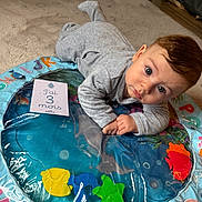 Nolan participe au concours pour gagner de l'argent avec cette photo : baby, infant, play_mat, grey_onesie, blue_eyes, colorful_toys, carpet, floor, indoor, child, cute, portrait, lying_down, early_milestone, soft_lighting, home, young_baby, 3_months, curious, playtime
