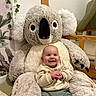 baby, smile, stuffed_animal, koala, plush, indoor, child, cute, happy, toy, seated, clothing, sweater, pants, face, person, home, decor, furniture, infant