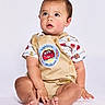 toddler, child, baby, sitting, clothing, shorts, shirt, lightning_mcqueen, cartoon, cute, studio, portrait, barefoot, expression, face, hands, legs, footwear_free, curious, innocent