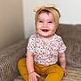 baby, barefoot, child, clothing, couch, cozy, cute, floral_shirt, happy, headband, home, indoor, infant, person, portrait, sitting, skin, smiling, toddler, yellow_pants