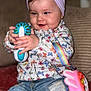 baby, casual, child, closeup, colorful, cute, floral_clothing, happy, headband, indoor, infant, jeans, person, pink_toy, playing, rainbow_strap, sitting, smiling, soft_furniture, toy