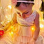 baby, blanket, child, curly_hair, cute, decorative_lights, dress, fairy_lights, flower, glowing, headband, indoors, peach, pink, portrait, sitting, soft_texture, toddler, warm_lighting, young_child