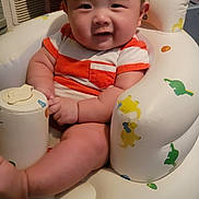 Alex is registered to the contest to win money with this photo: arm, baby, carpet, child, chubby, clothing, cute, dinosaur_print, face, happy, home, indoor, infant, inflatable_chair, leg, person, red_and_white_stripes, seated, smile, toy