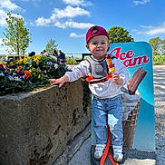 Kaison joined the competition — help win amazing prizes! toddler, child, red_cap, popsicle, flowers, stone_planter, advertisement, ice_cream, outdoor, daylight, blue_sky, clouds, jeans, white_sneakers, casual_clothing, playful, smiling, nature, bench, gravel_path