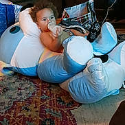 Loki joined the competition — help win amazing prizes! baby, infant, child, curly_hair, bottle, feeding, sitting, cushions, pillows, blanket, plush_toy, indoor, living_room, rug, carpet, couch, household, portrait, relaxed, colorful