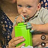 adult_hand, baby, birthday_candles, blue_paint, celebration, child, closeup, clothing, curious, face, finger_in_mouth, floral_pattern, glasses, green_container, hands, indoor, paint, party, person, table