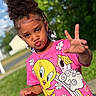 child, girl, curly_hair, pink_tshirt, tweety_bird, outdoor, greenery, sunny, pavement, playful, pout, hand_gesture, summer, casual_clothing, nature, portrait, young, happy, daylight, fun