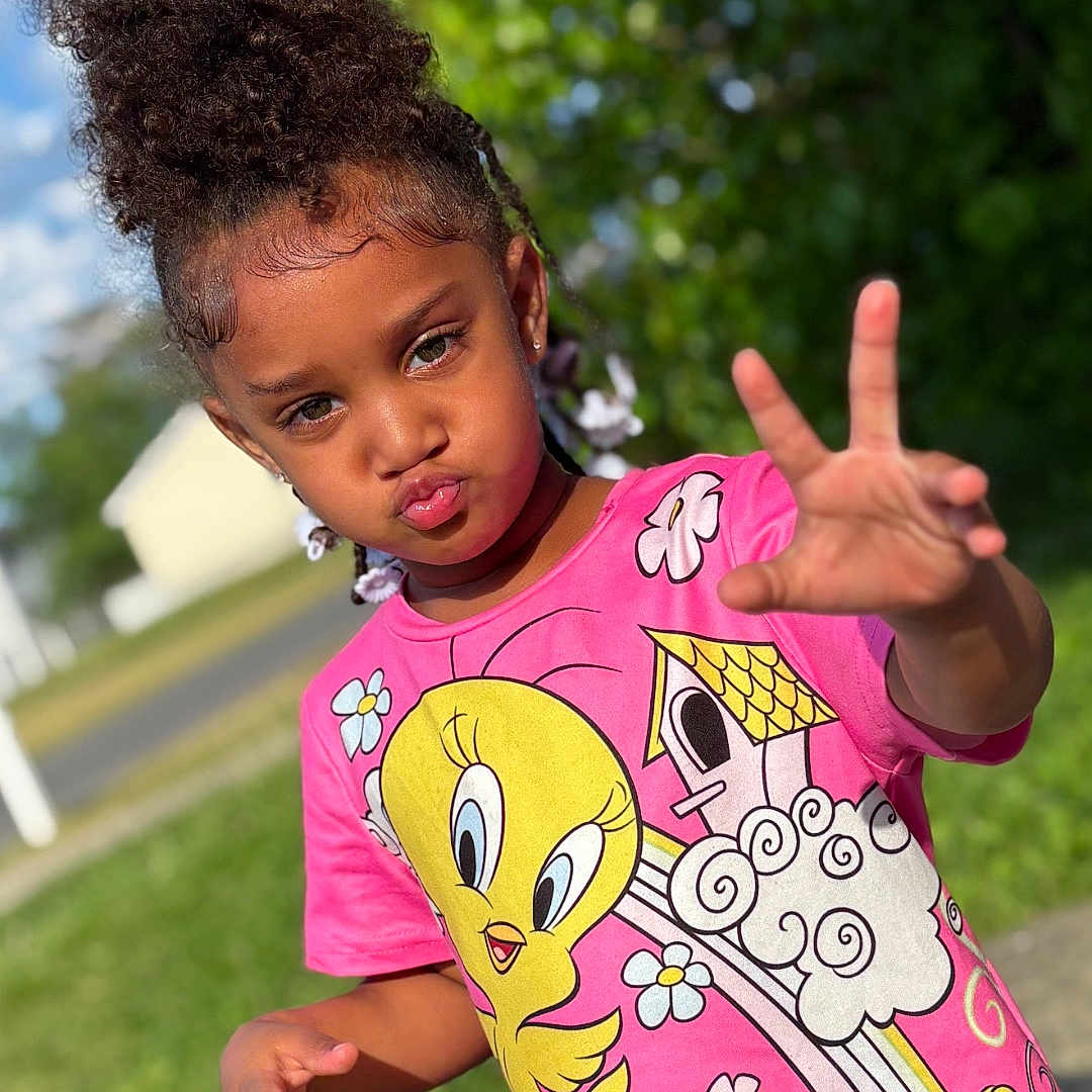 Ivionna joined the competition — help win amazing prizes! child, girl, curly_hair, pink_tshirt, tweety_bird, outdoor, greenery, sunny, pavement, playful, pout, hand_gesture, summer, casual_clothing, nature, portrait, young, happy, daylight, fun