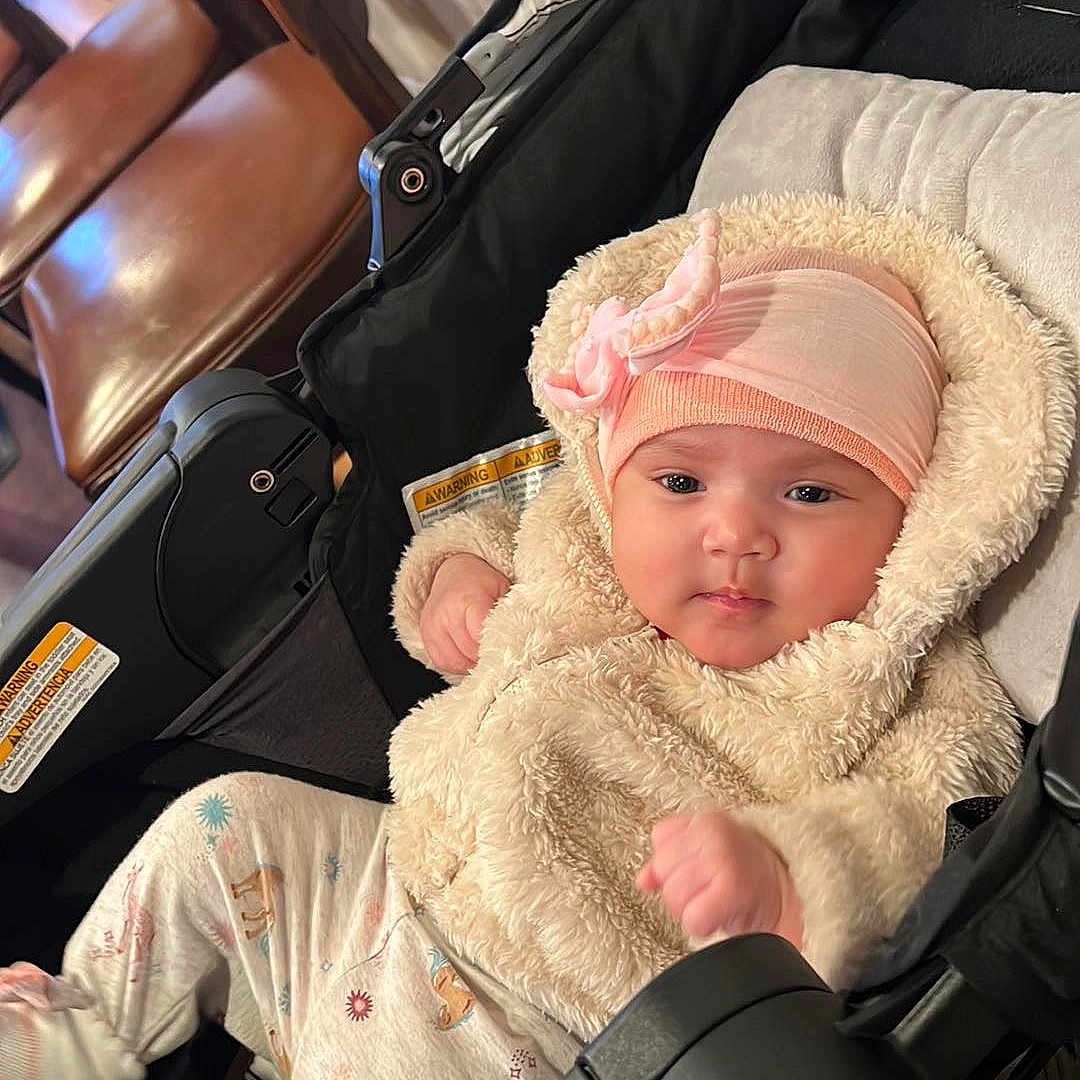 Yusra joined the competition — help win amazing prizes! baby, chair, child, clothing, cream, cute, fluffy, footwear, furniture, hat, indoor, infant, jacket, person, pink, portrait, relaxed, seat, stroller, wood