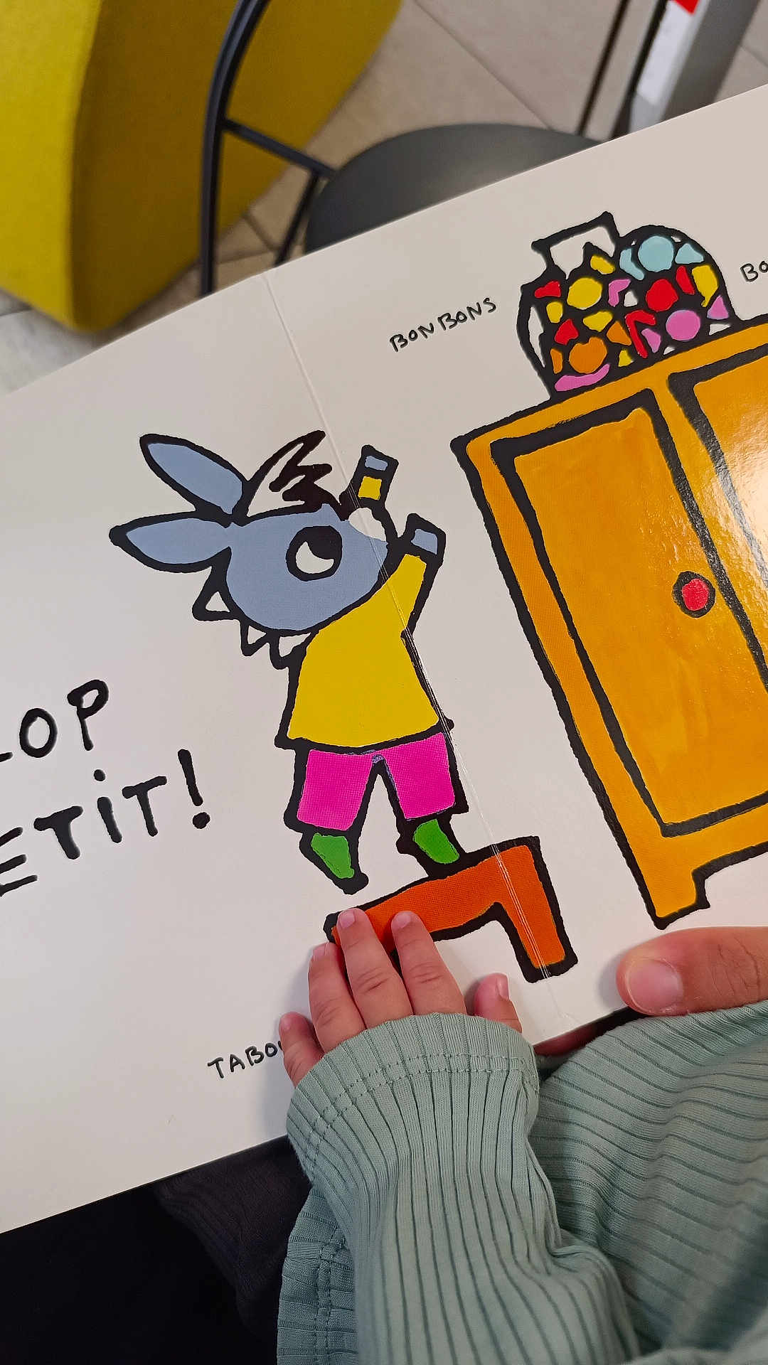Musab participe au concours pour gagner de l'argent avec cette photo : bonbons, book, cabinet, cartoon, child, childrens_book, colorful, cozy, curiosity, fingers, green_sleeve, hand, illustration, indoor, orange, reading, sitting, story, toy, young_child