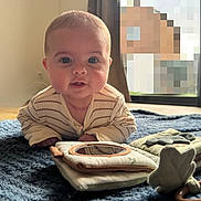 Gabriel a rejoint le concours — aidez-le/la à gagner de superbes lots ! baby, blue_blanket, child, clothing, curtain, eyes, face, floor, home, indoors, infant, leaf_toy, natural_light, plush_book, portrait, smiling, striped_shirt, toy, window, wooden_floor