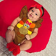 Rachell is registered to the contest to win money with this photo: baby, infant, smiling, red_headband, red_socks, brown_outfit, turkey_design, cushion, red_cushion, quilted_bedspread, cute, happy, lying_down, indoors, child, person, headband, sock, plush, apparel