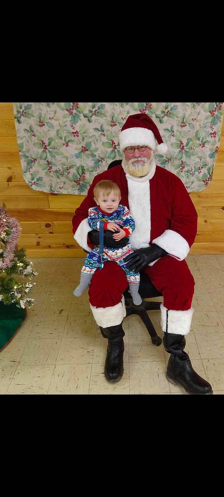 Elisha is registered to the contest to win money with this photo: baby, boot, christmas, christmas_eve, costume_hat, event, face, fictional_character, fun, happy, hat, headwear, holiday, lap, leg, person, plant, santa_claus, smile, sock