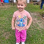 child, girl, outdoor, grass, pink_clothing, white_shoes, playful, standing, messy_face, casual, backyard, trees, person, stitch_tshirt, pants, smiling, hands_on_hips, dirt, daylight, man
