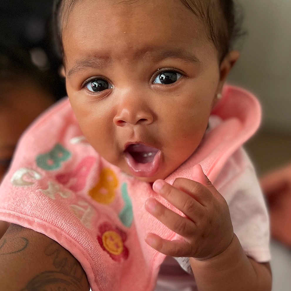 Je'Maya joined the competition — help win amazing prizes! baby, bib, blue_bow, child, closeup, clothing, curious, cute, expression, face, hand, indoor, infant, person, pink_bow, portrait, sitting, skin, tattoo, young_child