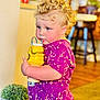 toddler, child, curly_hair, purple_shirt, yellow_cup, indoor, plant, wooden_floor, furniture, drinking, cute, person, face, diaper, home, casual, colorful, young_child, blonde_hair, standing