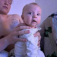 Damon joined the competition — help win amazing prizes! baby, adult, pajamas, blanket, hand, tattoo, bedroom, person, indoor, sleepy, expression, holding, face, skin, comfort, quilt, young, blue_eyes, clothing, bed