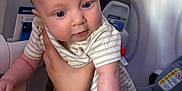 Damon is registered to the contest to win money with this photo: baby, infant, child, airplane, seat, hand, striped_clothing, person, interior, travel, transportation, car_seat, safety_card, curious, blue_eyes, holding, human, cabin, closeup, cute