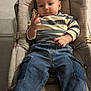 baby, child, infant, person, face, clothing, striped_shirt, denim_pants, cushion, seated, indoor, floor_tiles, cute, small_hands, expression, casual_wear, comfortable, relaxed, young, portrait