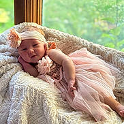 Gianna joined the competition — help win amazing prizes! baby, infant, pink_dress, headband, flower, blanket, soft_texture, window, natural_light, greenery, indoor, portrait, smiling, cute, child, relaxed, cozy, tulle, fabric, baby_fashion