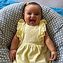 baby, child, smiling, yellow_dress, polka_dot, cushion, happy, indoor, portrait, infant, cute, person, sitting, soft_fabric, comfortable, headband, furniture, closeup, joy, skin
