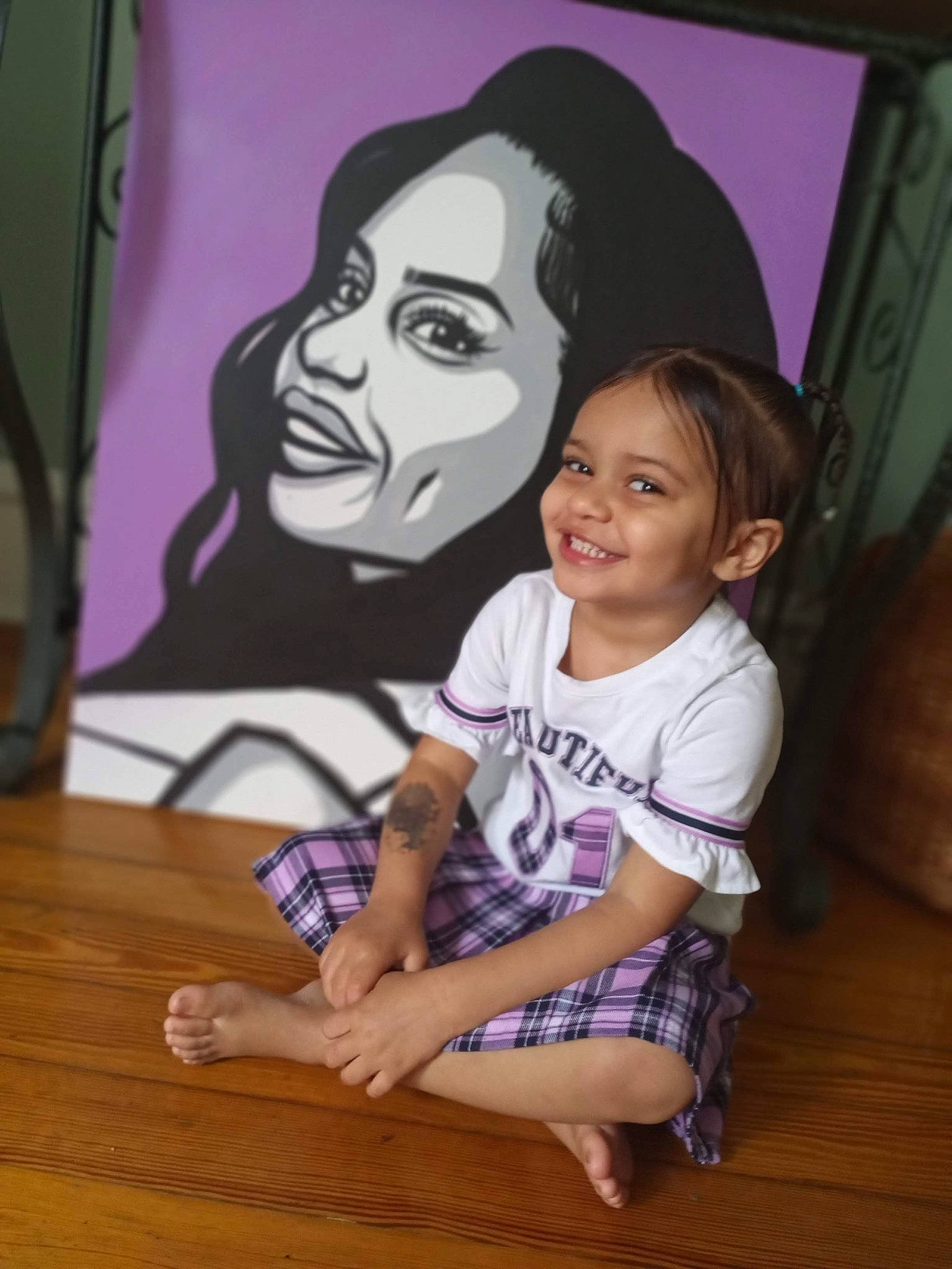 Emma joined the competition — help win amazing prizes! art, artist, child, flooring, fun, happy, hardwood, joy, magenta, painting, person, picture_frame, pink, sandal, shorts, sitting, smile, t_shirt, table, toddler