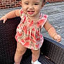 toddler, child, smiling, standing, wicker_chair, wooden_deck, brick_wall, window, dress, watermelon_pattern, white_shoes, earring, bracelet, outdoor, happy, cute, person, face, baby, summer